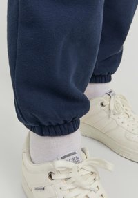 Navy blue joggers made of soft fabric with elastic cuffs, paired with white sneakers featuring a textured surface and visible brand logo.