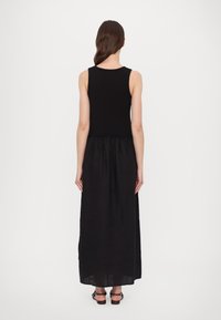 Robe noire sans manches avec un haut ajusté et une jupe longue fluide. Le tissu est lisse avec une taille froncée et un design simple.