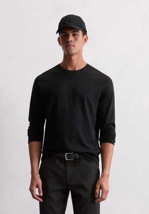 Zwarte long sleeve shirt met een ronde hals, gecombineerd met zwarte broeken en een bijpassende zwarte pet met een logo aan de voorkant.