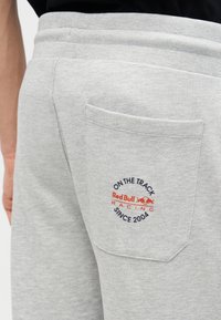 Τσέπη γκρι φόρμας με λογότυπο Red Bull Racing και κείμενο «Στον αγώνα από το 2004», που φοράει άτομο με μαύρο πουκάμισο.