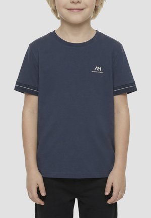 Enfant portant un t-shirt bleu marine à manches courtes avec un petit logo blanc sur la poitrine gauche et un pantalon noir, debout sur un fond clair.