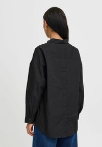 Čierna oversized košeľa na gombíky z ľahkej tkaniny, s dlhými rukávmi, klasickým golierom a rovnou zadnou páskou.