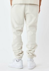 Pantalones joggers de un suave beige claro con un acabado texturizado, que presentan puños elásticos y un corte relajado, combinados con zapatillas blancas.
