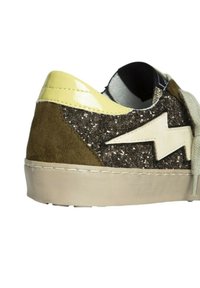 Zapatilla con parte superior de ante marrón y verde, acentos brillantes, tacón de charol amarillo y suela color crema; presenta un diseño de rayo blanco.