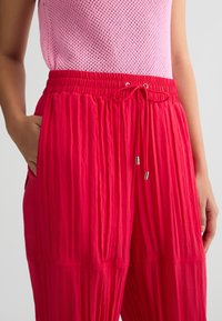 Pantaloni rossi larghi con una superficie testurizzata e vita elasticizzata. Presentano tasche laterali e un cordoncino con estremità in tonalità argento.