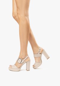 Sandales à plateforme beiges à talons hauts avec une large lanière ornée d'une grande boucle en argent, design à bout ouvert et talon épais.