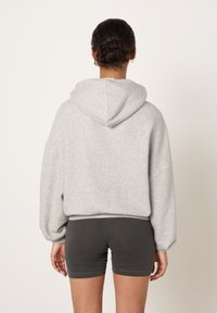 Siva kratka jopa s kapuco, s sproščenim krojem in spuščenimi rameni, združena s temno sivimi kratkimi hlačami. Gladek otip.