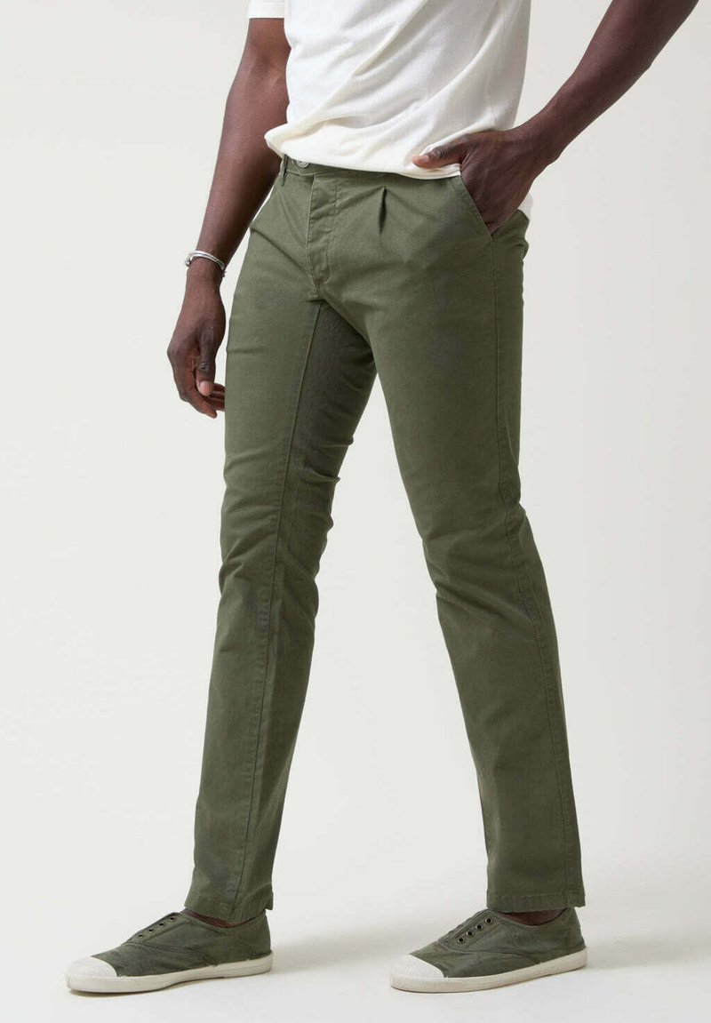 Pantalones ajustados de color verde oliva hechos de algodón, con un frente plano, bolsillos laterales y un diseño limpio. Combinados con zapatillas bajas grises.