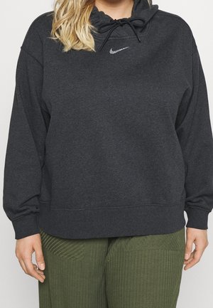 Personne portant un sweat à capuche Nike gris foncé avec cordon de serrage et un pantalon côtelé vert olive, debout les mains relâchées le long du corps.