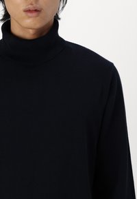 Suéter de cuello alto en azul marino con un diseño ajustado. Confeccionado en una suave tela de punto, presenta un cuello alto y mangas largas para mayor calidez.