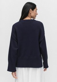 Marinblå stickad tröja med ribbad nederkant och ärmar, som har en avslappnad passform och rundad halsringning, samt synliga sömdetaljer på baksidan.