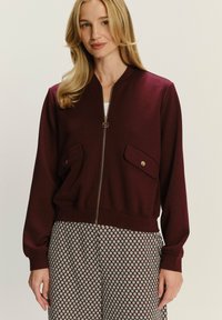 Bordeaux ritsjack met twee voorzakken, geribde manchetten en zoom, gemaakt van zachte stof voor een comfortabele pasvorm.