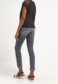 Top nero con design a spalline scoperte, jeans skinny grigi e sandali neri con dettagli a strappo. Jeans con risvolti.