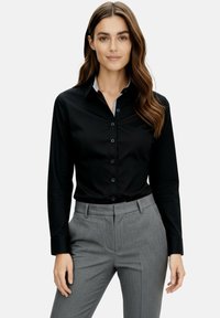 Black button-up shirt with long sleeves and a striped collar, paired with tailored gray trousers, featuring a smooth fabric and fitted design.