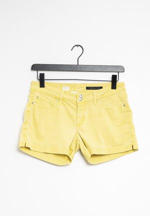 Gele denimshorts met voorzakken en dubbele zilveren knopen, hangend aan een zwarte kleerhanger tegen een witte achtergrond.