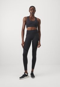 Conjunto deportivo negro que incluye un sujetador deportivo ajustado con tejido texturizado y leggings de cintura alta con paneles de acento, complementado con zapatillas negras.
