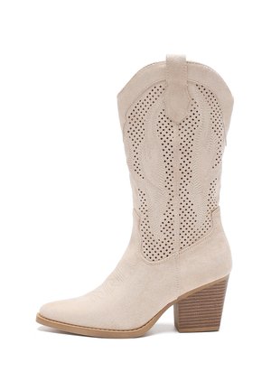 Beige suede cowboy boot with pointed toe, cut-out design, intricate stitching, and a stacked heel. Textured surface and western accents.