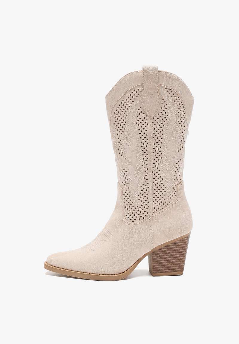 Bota vaquera de ante beige con punta afilada, diseño recortado, costuras intrincadas y tacón apilado. Superficie texturizada y acentos western.