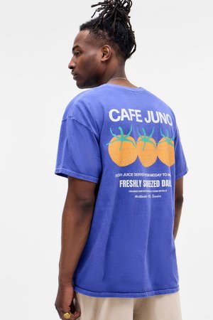Fialové bavlnené tričko s grafikou pomarančov s zelenými listami, s nápisom „CAFE JUNO“ a detailmi služby vytlačenými na bielo. Krátke rukávy.