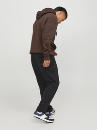 Sudadera marrón con cordón, combinada con pantalones de chándal azul marino oscuro. Zapatillas negras, blancas y azules completan el atuendo.