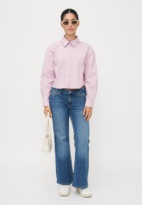 Striped pink button-up shirt, blue flared jeans, white sneakers, and a small white handbag. The shirt features a classic collar and long sleeves.