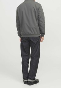 Gray bomber jacket with ribbed cuffs, paired with dark blue denim jeans featuring contrasting stitching and black loafers.