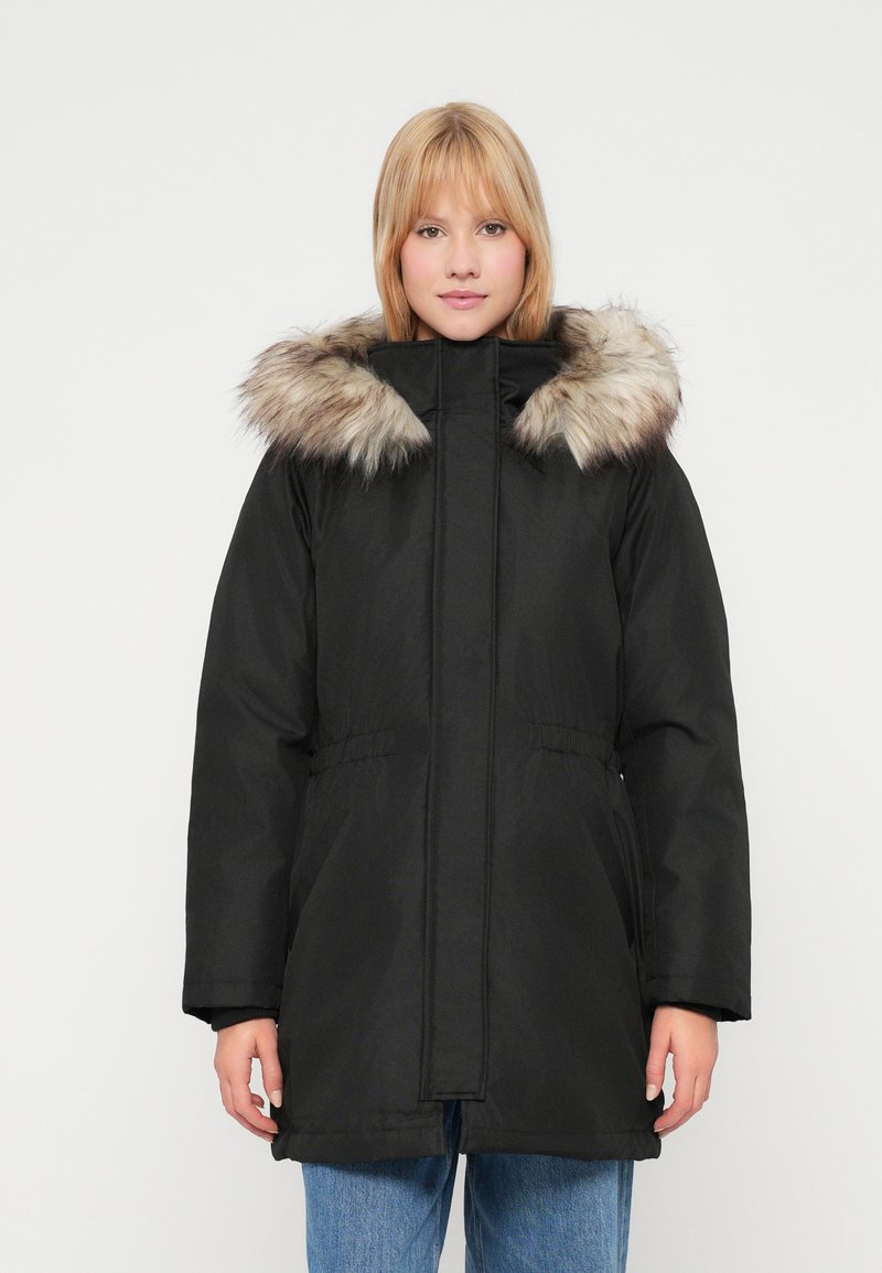 Czarna parka z kapturem wyłożonym futrem, z zamkiem błyskawicznym, kieszeniami po bokach i elastycznym wykończeniem w talii. Tkanina ma gładką teksturę.