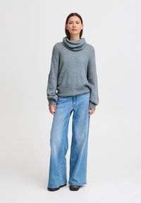 Maglione con collo a cowl in morbido tessuto grigio, abbinato a jeans blue a gamba larga. L'outfit presenta vestibilità rilassate e un design minimalista.