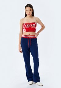 Top corto rojo y blanco con el texto "CHICAGO", combinado con pantalones de chándal azules con cordón y franjas blancas a los lados. Se muestran zapatillas blancas.