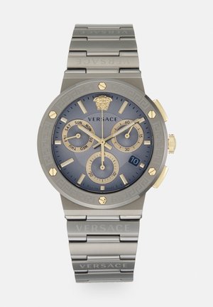 Montre Versace avec un cadran bleu, des accents dorés, des fonctions chronographe et un bracelet en métal gris comportant le nom de la marque gravé et un motif de clé grecque.