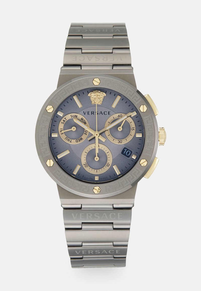 Versace-Uhr mit blauem Zifferblatt, goldenen Akzenten, Chronographenfunktionen und grauem Metallarmband mit eingraviertem Markennamen und griechischem Schlüssel-Muster.
