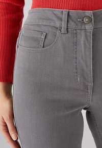 Pantalones de mezclilla grises con cintura alta y corte ajustado. Presentan un bolsillo frontal, trabillas para el cinturón y un cierre de botón. Textura suave y detalle de costura sutil.