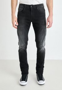 Black denim jeans with a slim fit, featuring a faded wash, five pockets, and a button closure. Paired with black and white sneakers.