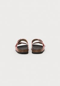 Sandales rouges avec deux brides réglables, semelle en liège et semelle noire texturée. Comprend des franges décoratives et des accents en métal argenté.