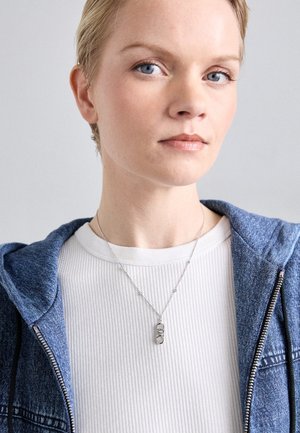 Hõbedane kaelakee ovaalse ripatsi ja tekstuuri kujundusega, kantud valge ribakujulise särgi ja sinise teksajaki peal.