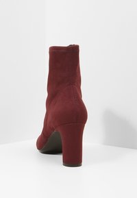 Burgundské kotníkové boty z měkké semišové kůže s kulatou špičkou a blokovým podpatkem o výšce 7,5 cm. Obsahují hladký zadní šev a boční zip.