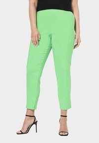 Pantalons verts extensibles à coupe slim, avec une texture lisse et longueur cheville. Associés à des talons noirs à lanières pour le contraste.