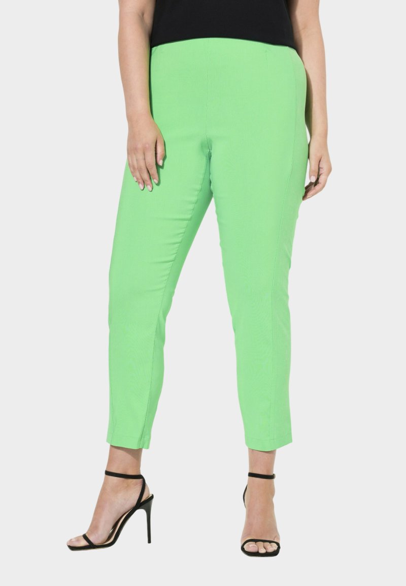 Pantalons verts extensibles à coupe slim, avec une texture lisse et longueur cheville. Associés à des talons noirs à lanières pour le contraste.