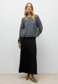 Siva pletena majica z sproščenim krojem in teksturirano tkanino, v paru z dolgim črnim krilom in svetlobrnimi čevlji na peto.