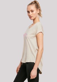 Beige t-shirt with short sleeves and a round neckline. Features colorful text design on the front. Loose fit, longer back hem.
