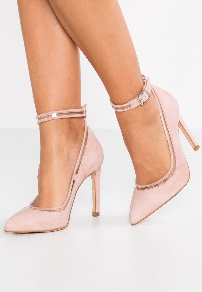 Escarpins en cuir suédé rose avec des pointes pointues et une bride de cheville transparente, présentant une silhouette élégante et de fins talons aiguille.