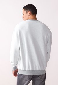 Felpa grigia con superficie testurizzata e polsini a coste. Presenta un collo rotondo e spalle basse, indossata con jeans grigi.