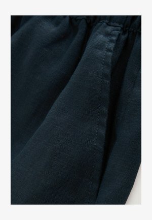 Tamsiai mėlyna medžiaga su tekstūruotu, audiniu dengtu paviršiumi; susiraukšlėjęs juosmens detalė; lygūs kraštai; lengvas audinys.