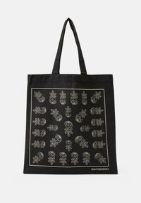 Svart totebag med hvitt blomsterdesign, som har konturer av blomster og blader, laget av slitesterkt stoff, med doble håndtak.
