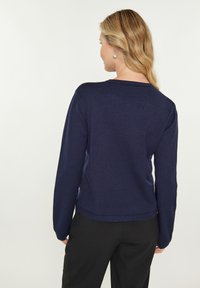 Pulover bleumarin cu mână lungă, cu un guler rotund și o textură netedă, având un design ușor ajustat în talie.