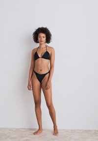 Black bikini featuring a triangular top and low-rise bottom, crafted from smooth fabric with adjustable straps and minimal detailing.