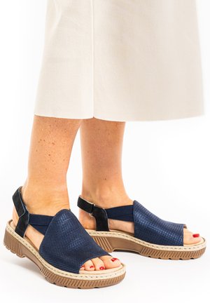 Navy open-toe sandals with textured upper, elastic straps, and a light brown rubber sole featuring a patterned design.