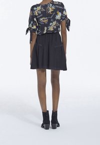 Abito corto nero con vita arricciata, abbinato a una blusa larga a fantasia con stampe di palme e animali, rifinita con maniche con lacci.