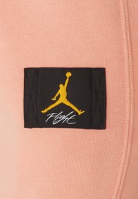 Pink fabric with a black tag featuring a yellow Jumpman logo and "Flight" text in white. Soft texture, rectangular tag, simple design.