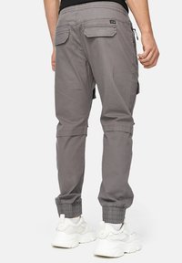 Cargo bukser i lysegrå stof med elastiske manchetter, baglommer og lynlåsdetalje på siden. Parret med hvide sneakers.